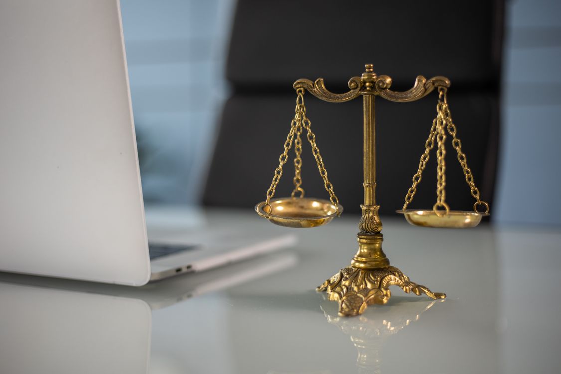 Waage der Justitia neben einem Laptop auf dem Schreibtisch — Symbol für die rechtlichen Grenzen der Direktansprache