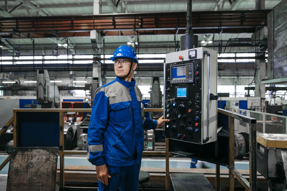 Produktionsleiter mit Schutzhelm an der Steuerung einer Werkzeugmaschine in einer Fertigungshalle