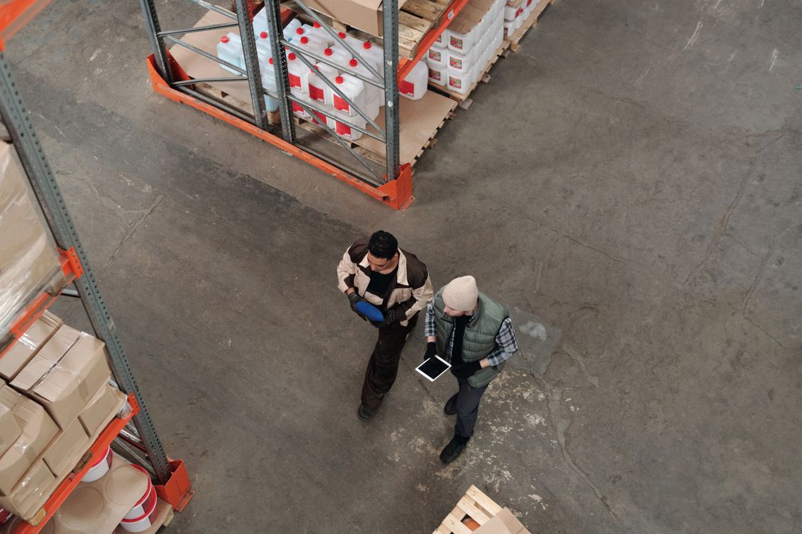 Zwei Mitarbeiter erfassen Lagerbestände mit einem Tablet zwischen Palettenregalen