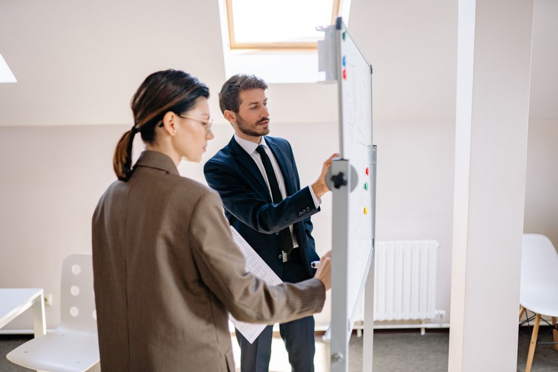 Zwei Führungskräfte entwerfen am Whiteboard die künftige Organisationsstruktur eines mittelständischen Unternehmens