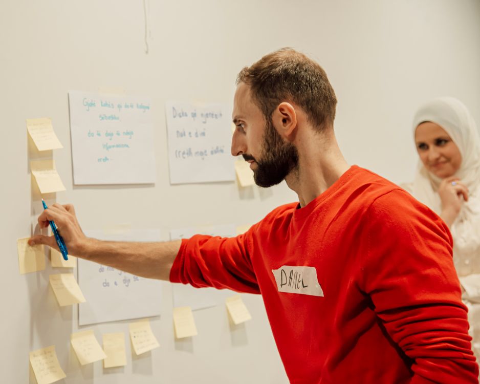 Mitarbeiter moderiert einen Teamentwicklungs-Workshop mit Notizzetteln an der Wand vor Kolleginnen und Kollegen