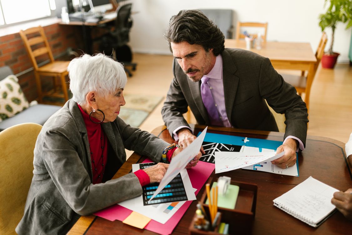 Seniorchefin und Berater sitzen am Besprechungstisch und gehen die Unterlagen zur Nachfolgeplanung durch