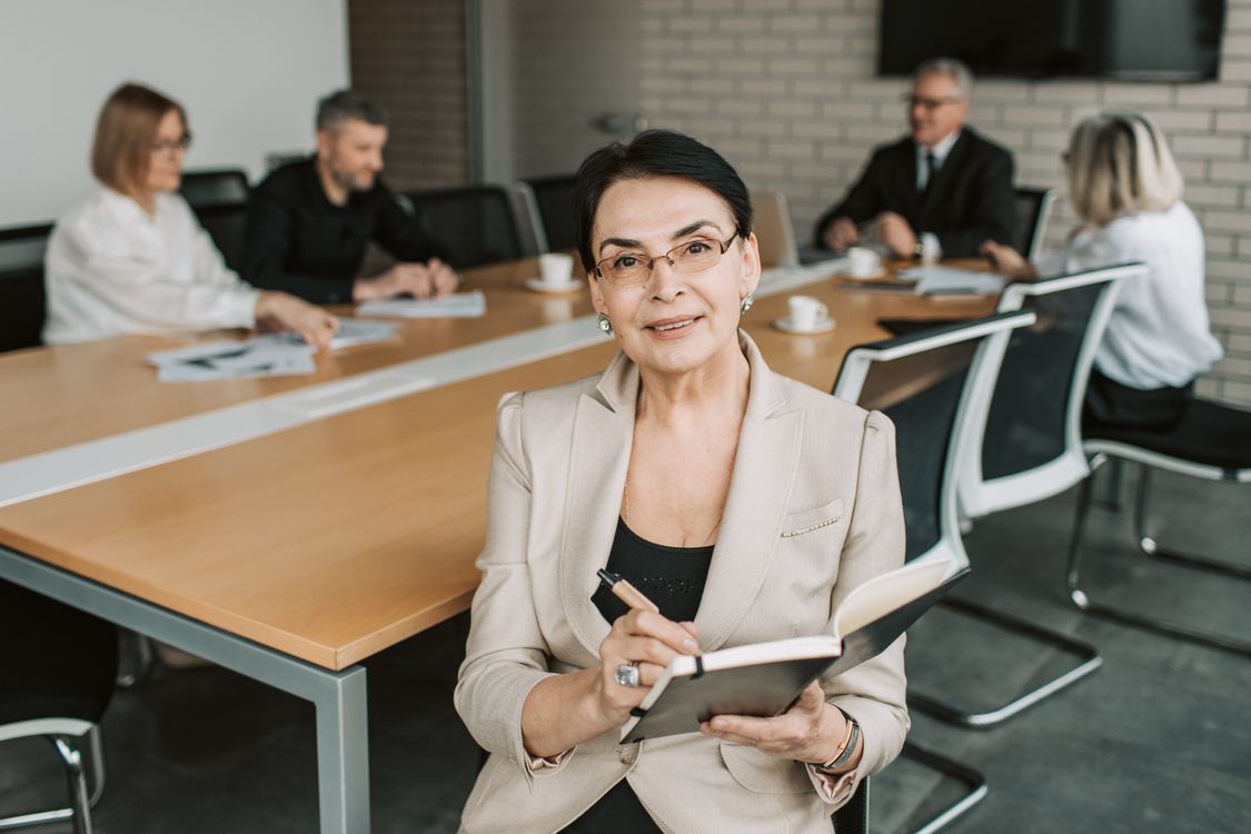 Führungskraft mit Notizbuch vor ihrem Team im Besprechungsraum eines mittelständischen Unternehmens
