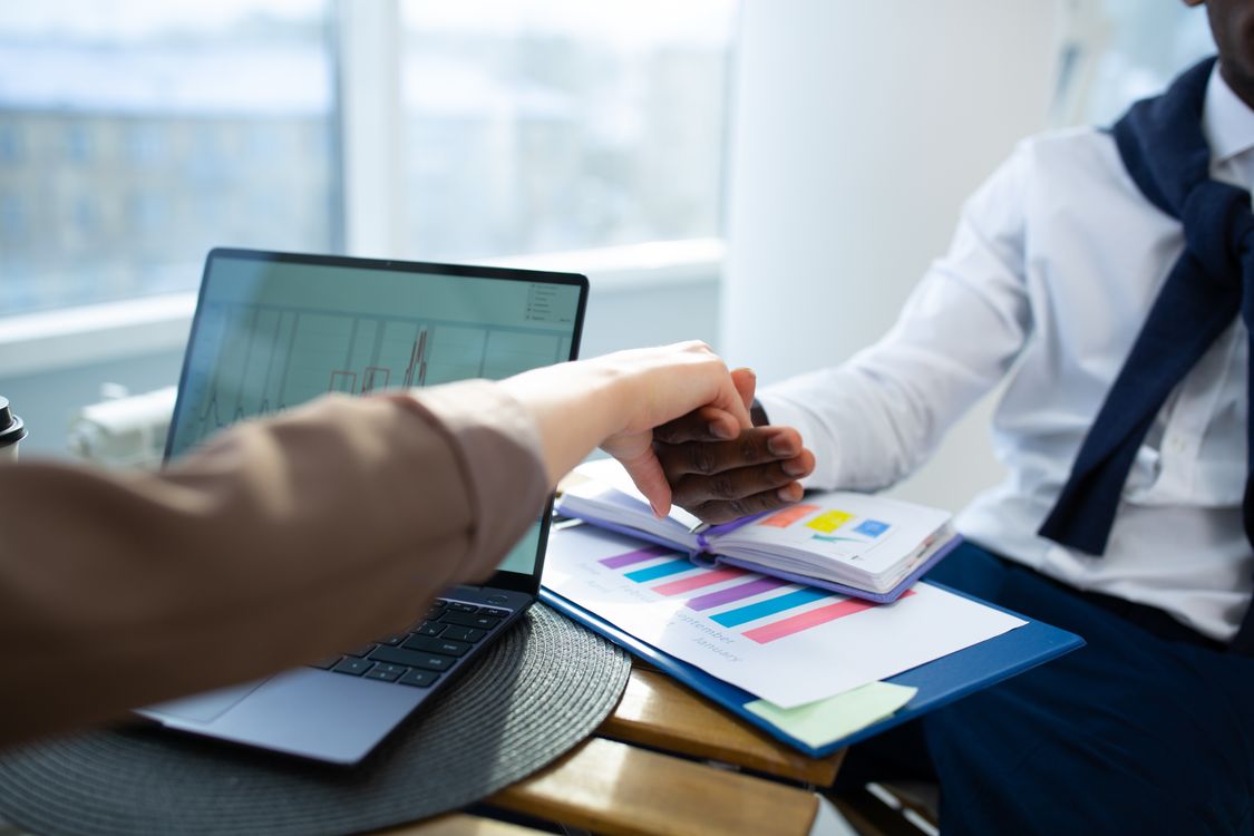 Zwei Geschäftspartner besprechen ein Angebot mit Diagrammen und Laptop am Tisch