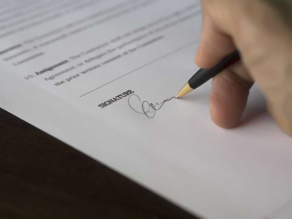 Hand unterschreibt einen Vertrag auf einem Schreibtisch