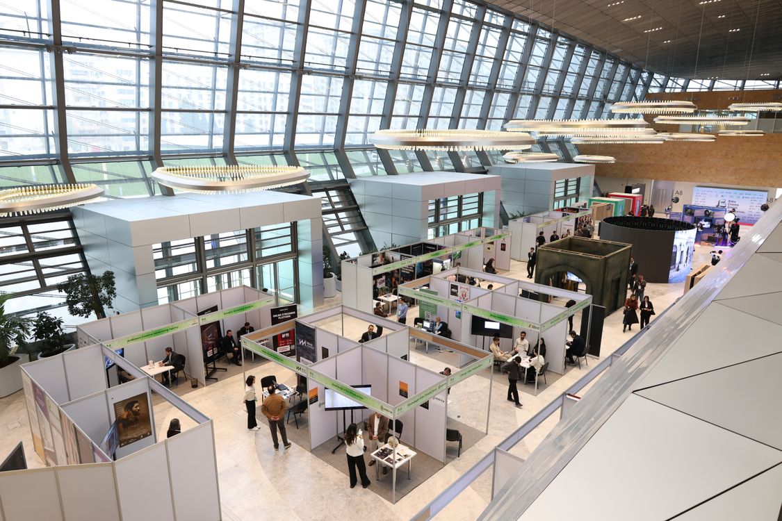 Blick von oben auf eine Messehalle mit Ständen und Besuchern im Gespräch