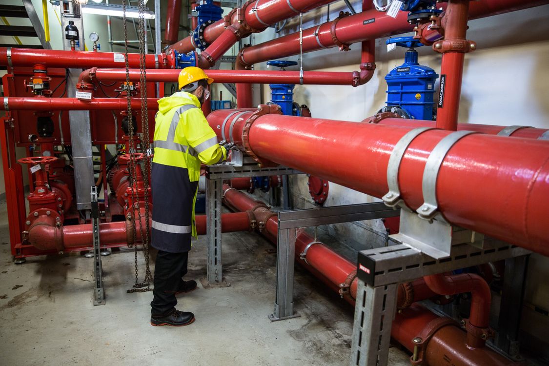 Anlagenfahrer in Warnschutzkleidung prüft rote Rohrleitungen und Armaturen in einer Chemieanlage